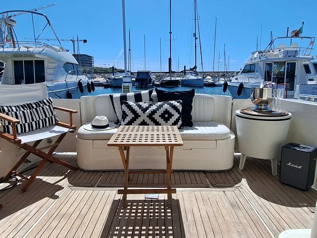Lounge area on a yacht deck with patterned cushions, overlooking a marina.