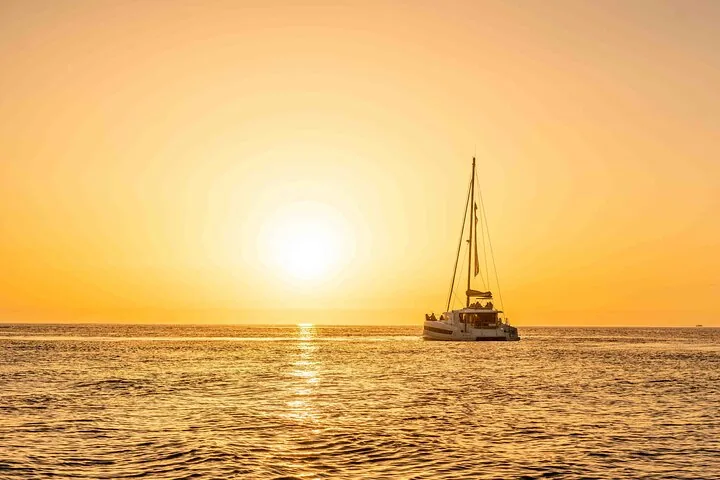 Catamaran sailing on a calm river during a golden sunset