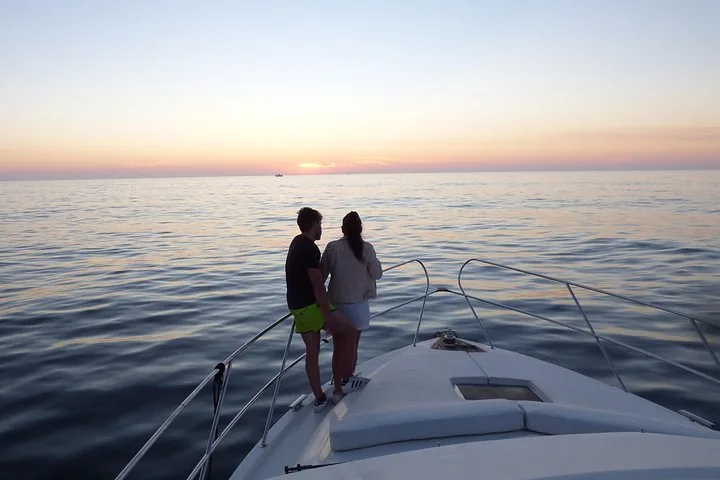 Couple standing on the bow of a yacht enjoying sunset views over the ocean.